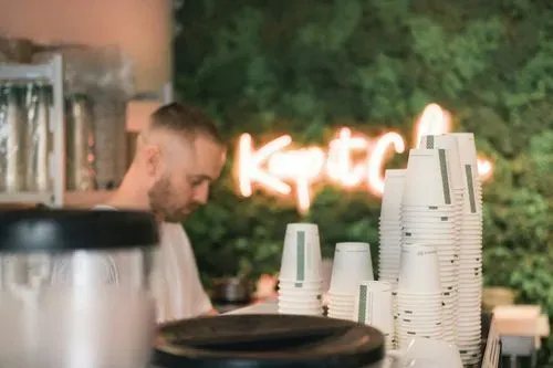 Barista working behind a stack of cups, with a neon sign in the background
