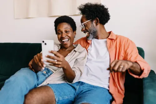 A joyful couple relaxes together on a cozy couch in their inviting living room, sharing smiles and laughter.