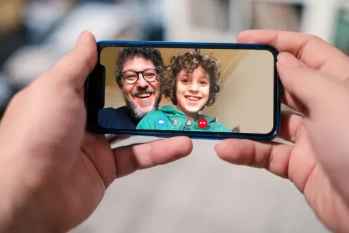 A man displays a cell phone showing a video of another man and his son, capturing a heartfelt moment.