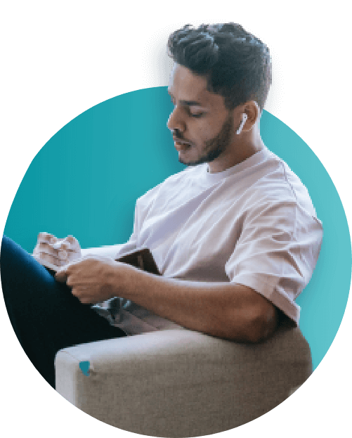 Man with earbuds seated, writing in notebook.