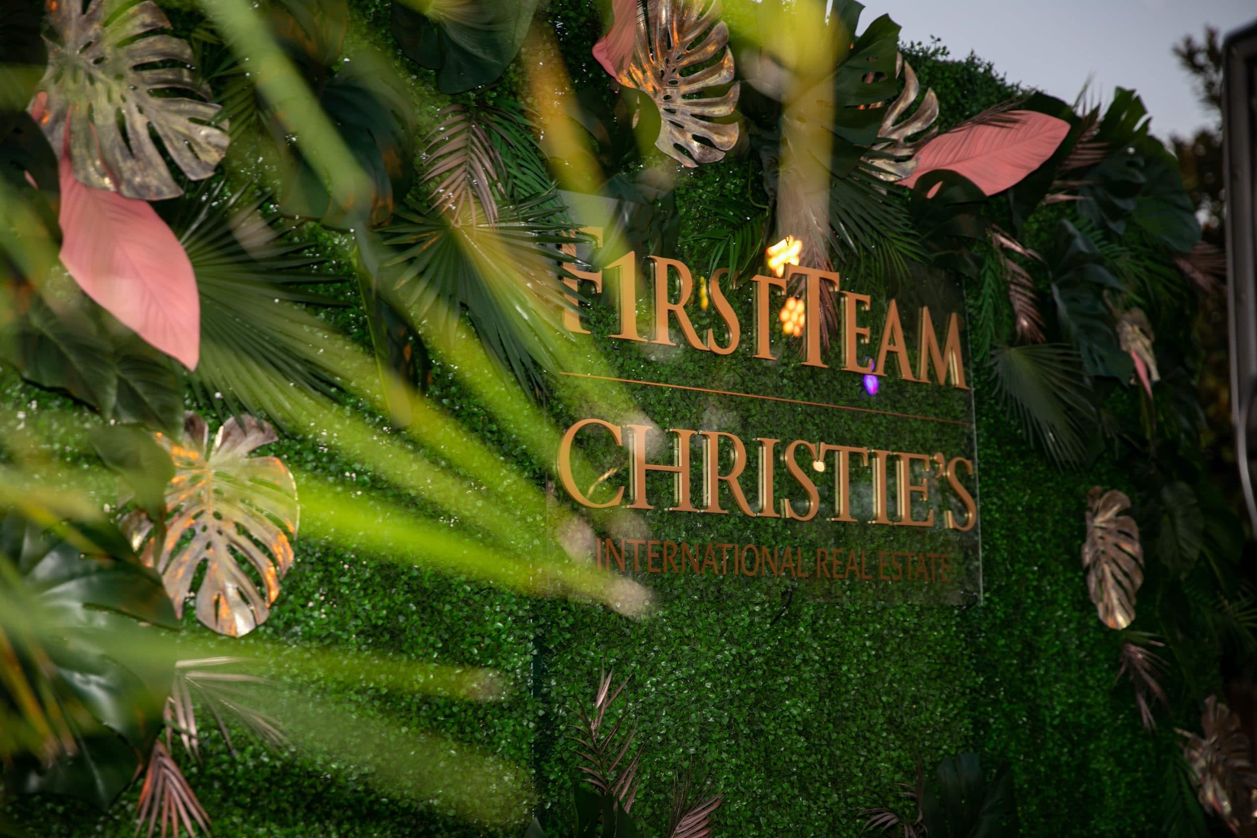 First Team Christie's logo on greenery wall with palm leaves
