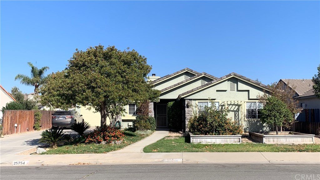 Home exterior with large tree, driveway and lush landscaping.