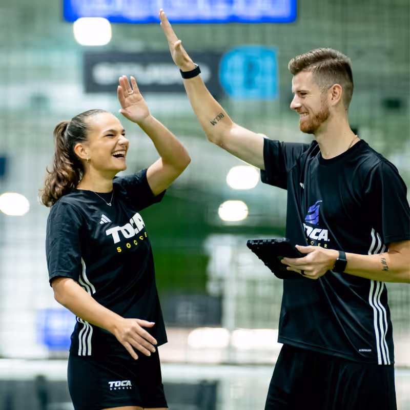 Soccer player and coach doing a high-five with technology enabled score board in background.