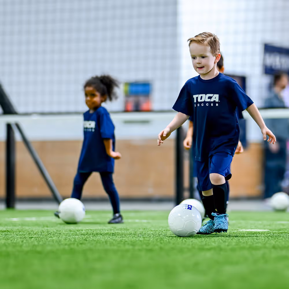 Two kids in soccer team pinnies going after ball