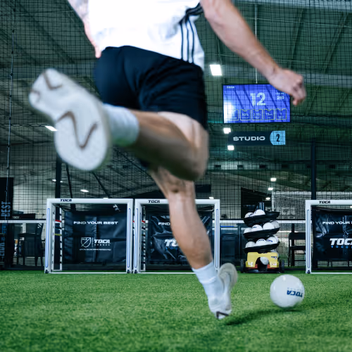 Soccer player in a private training session kicking the ball toward a TOCA technology-enabled goal on an indoor soccer field.