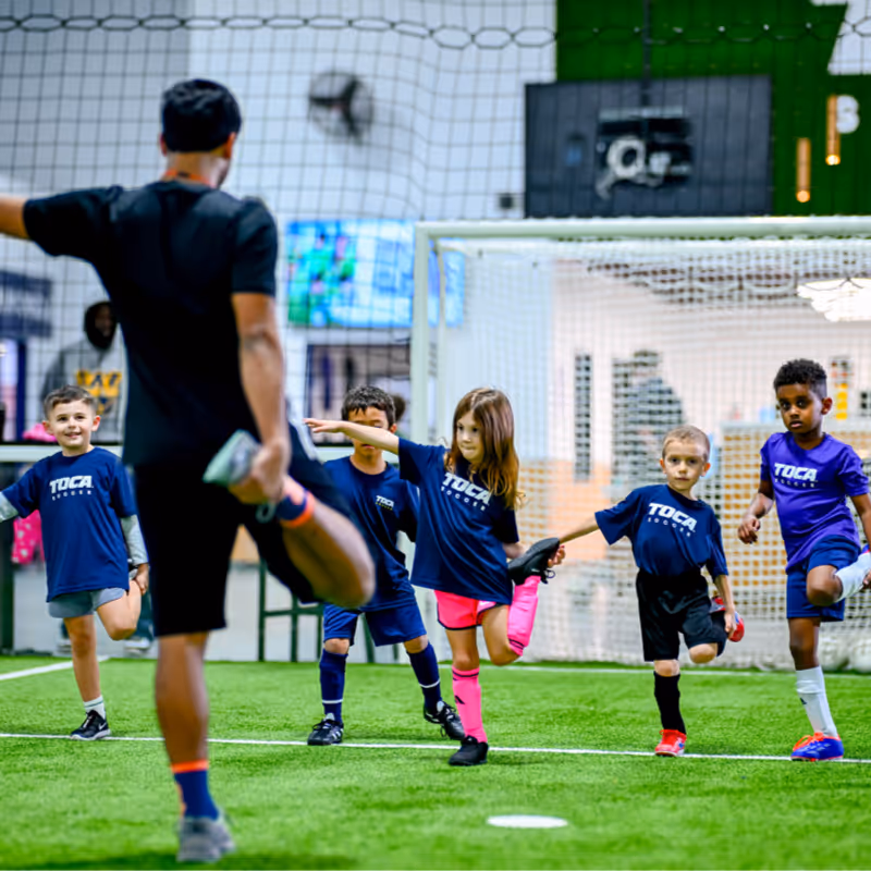 Kids at a TOCA Soccer class warming up before playing on the indoor soccer field.