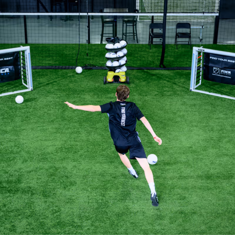 Player practicing during a TOCA technology enabled private soccer training session, kicking the ball on an indoor field.