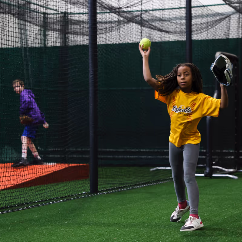 Young baseball player practicing ball throwing and catching in a TOCA indoor training facility, having fun while practicing and building skills.