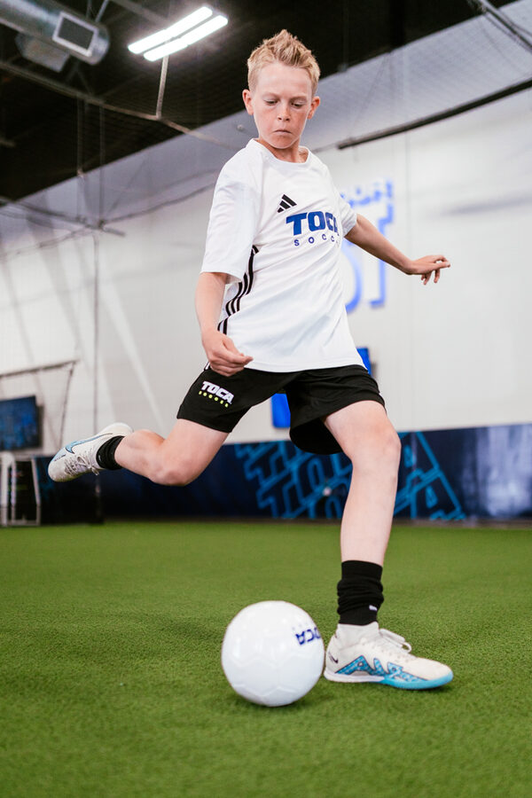 Youth soccer player preparing to kick soccer ball on indoor soccer field.