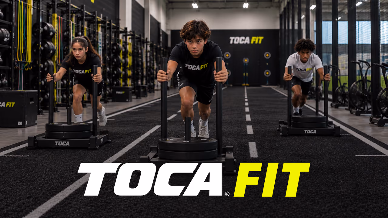 Three young people in a gym pushing weighted sleds on a black track with fitness equipment along the walls and the logo TOCA FIT overlaid at the bottom.