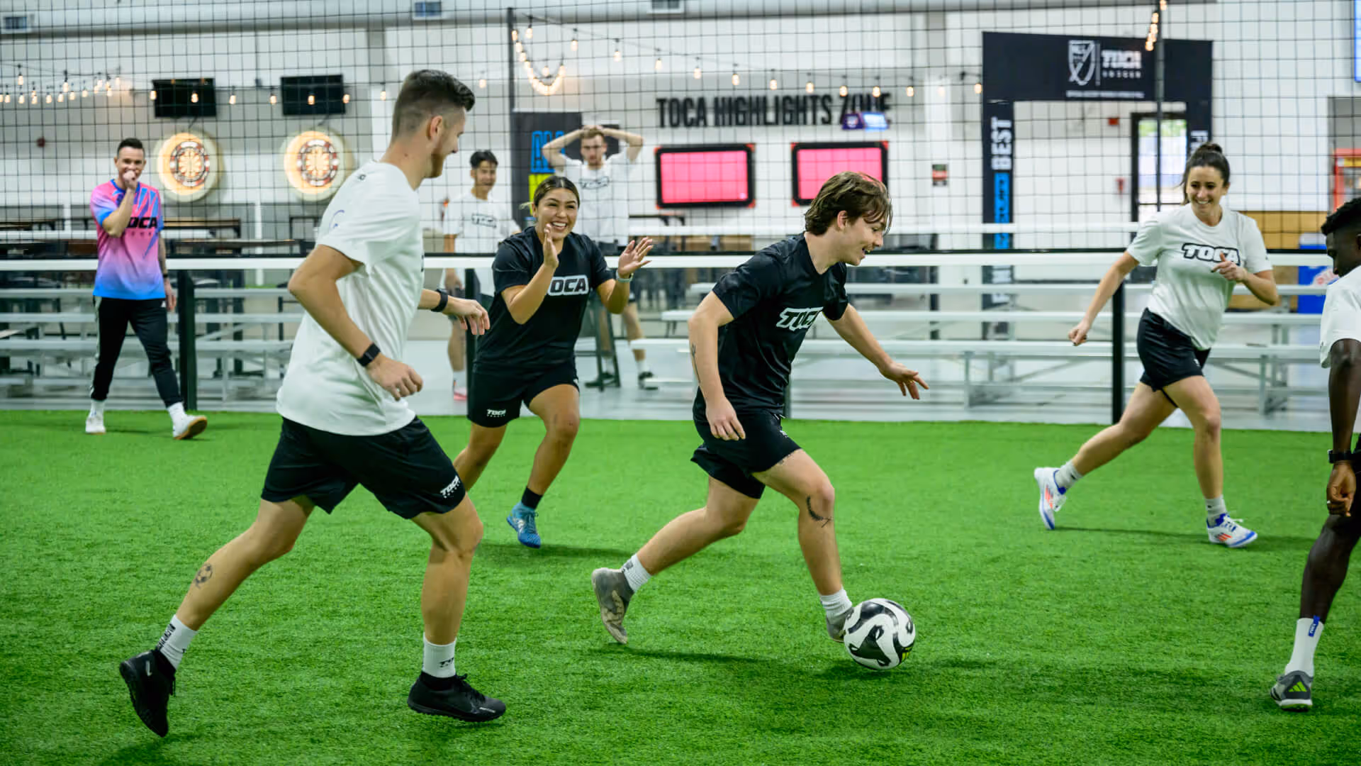 Soccer player dribbling the ball during an indoor league game with teammates running beside on an indoor turf field.