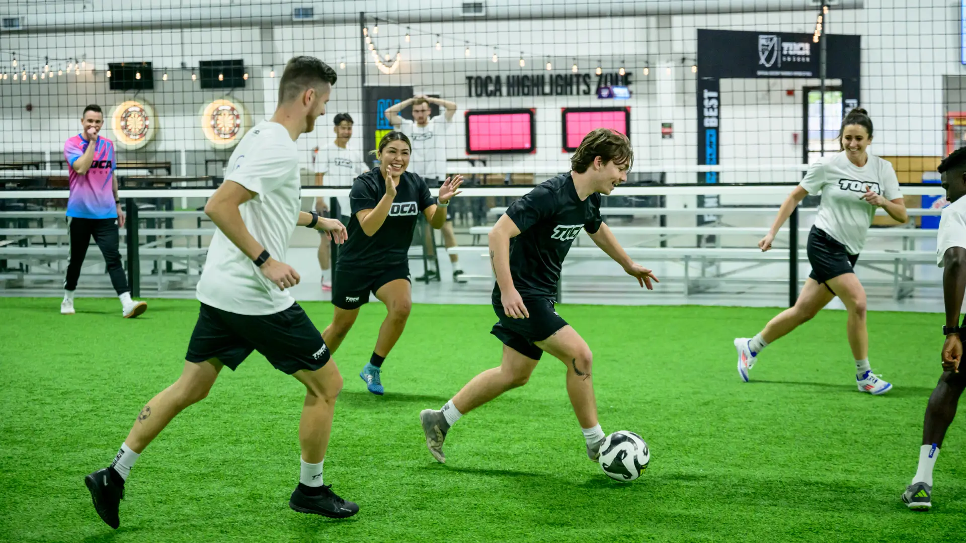Adult players competing in a coed indoor soccer league game on turf at a TOCA Soccer facility