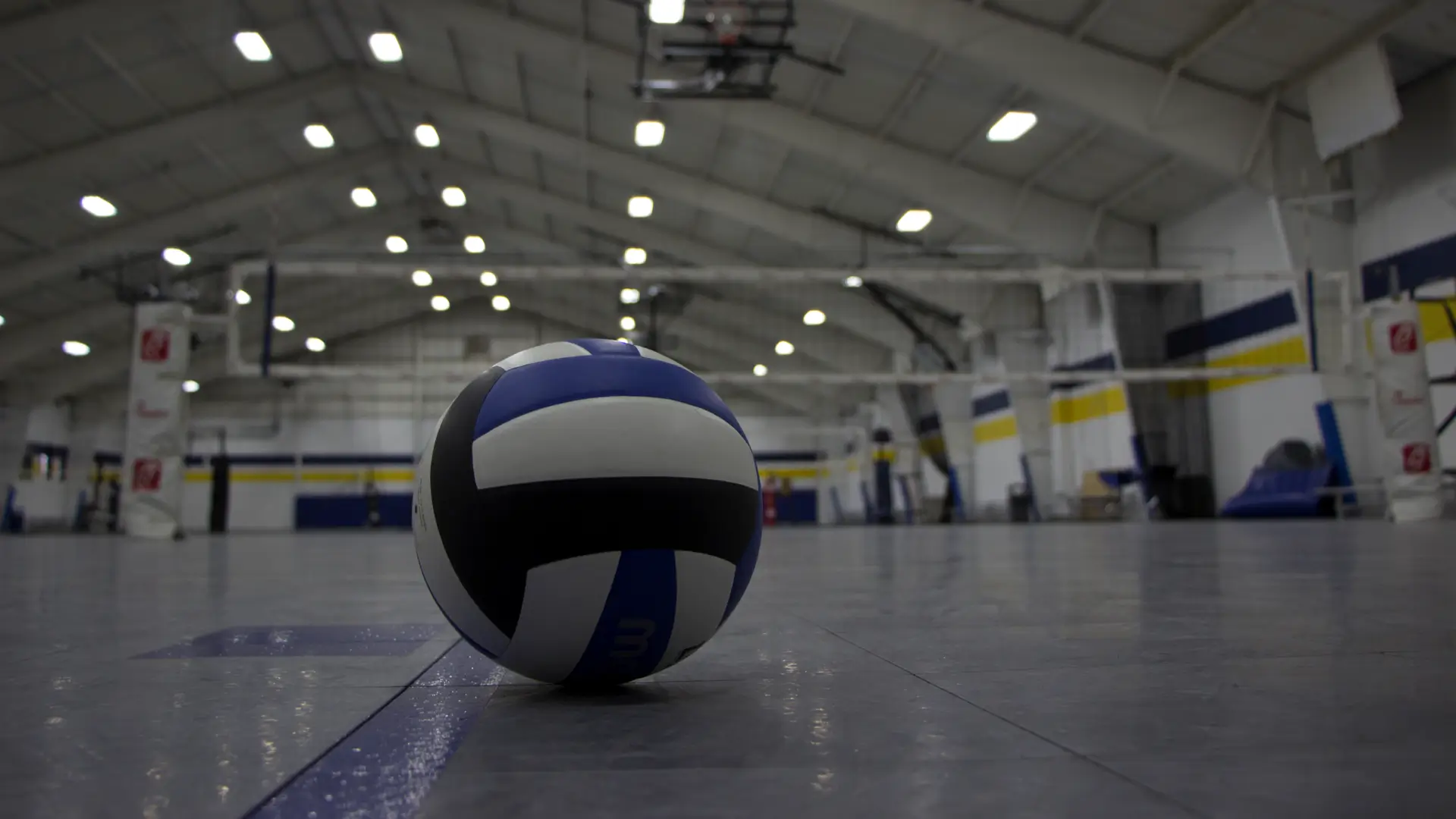 Volleyball resting on the floor of an indoor sports facility with nets and courts in the background