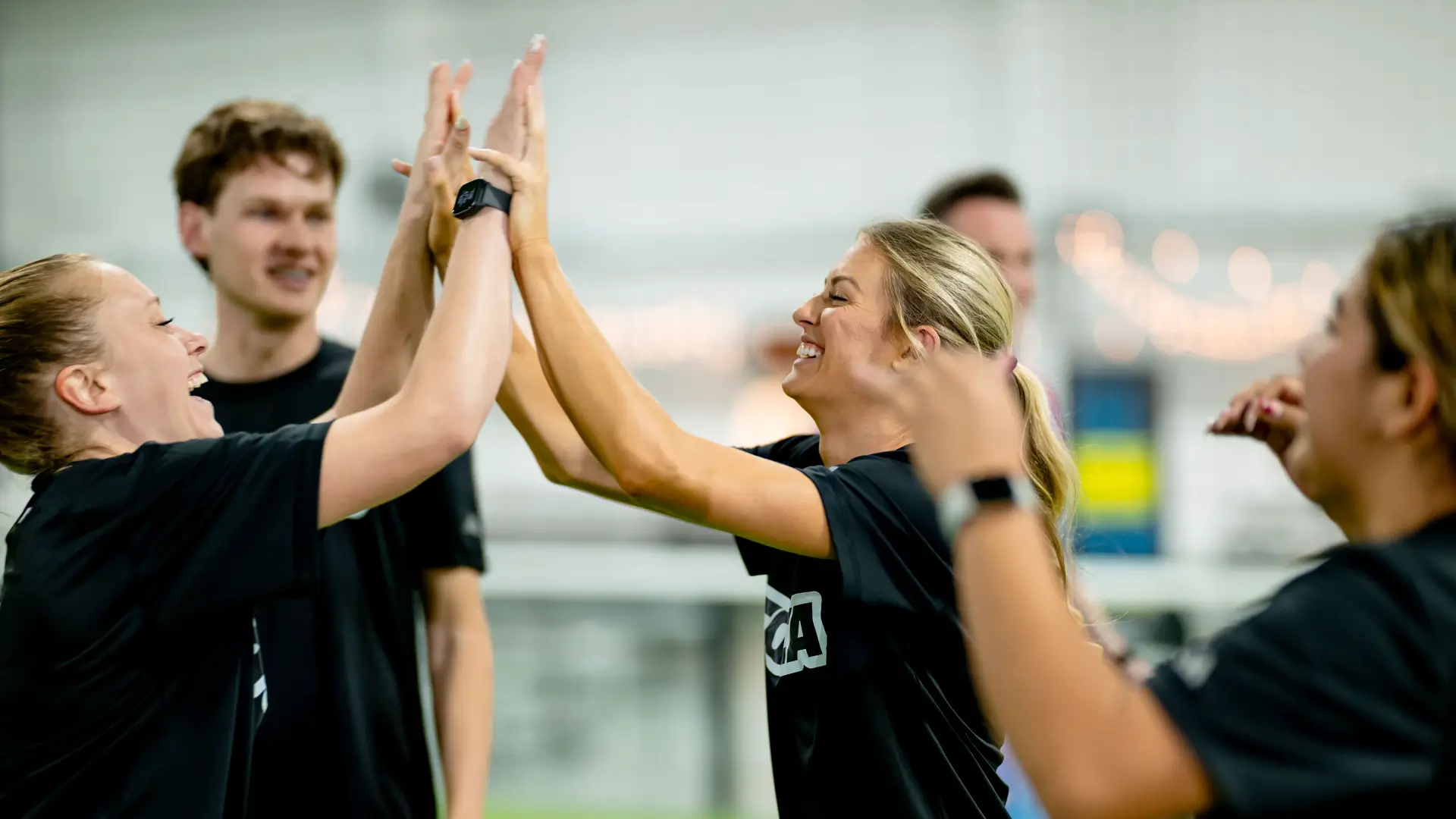 Adult soccer players in TOCA jerseys high-fiving and laughing together inside a TOCA Soccer facility