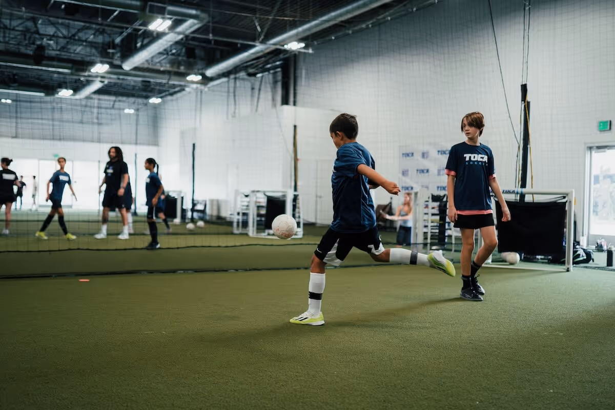 Youth soccer players in TOCA Soccer jerseys passing and moving on indoor turf during a soccer clinic