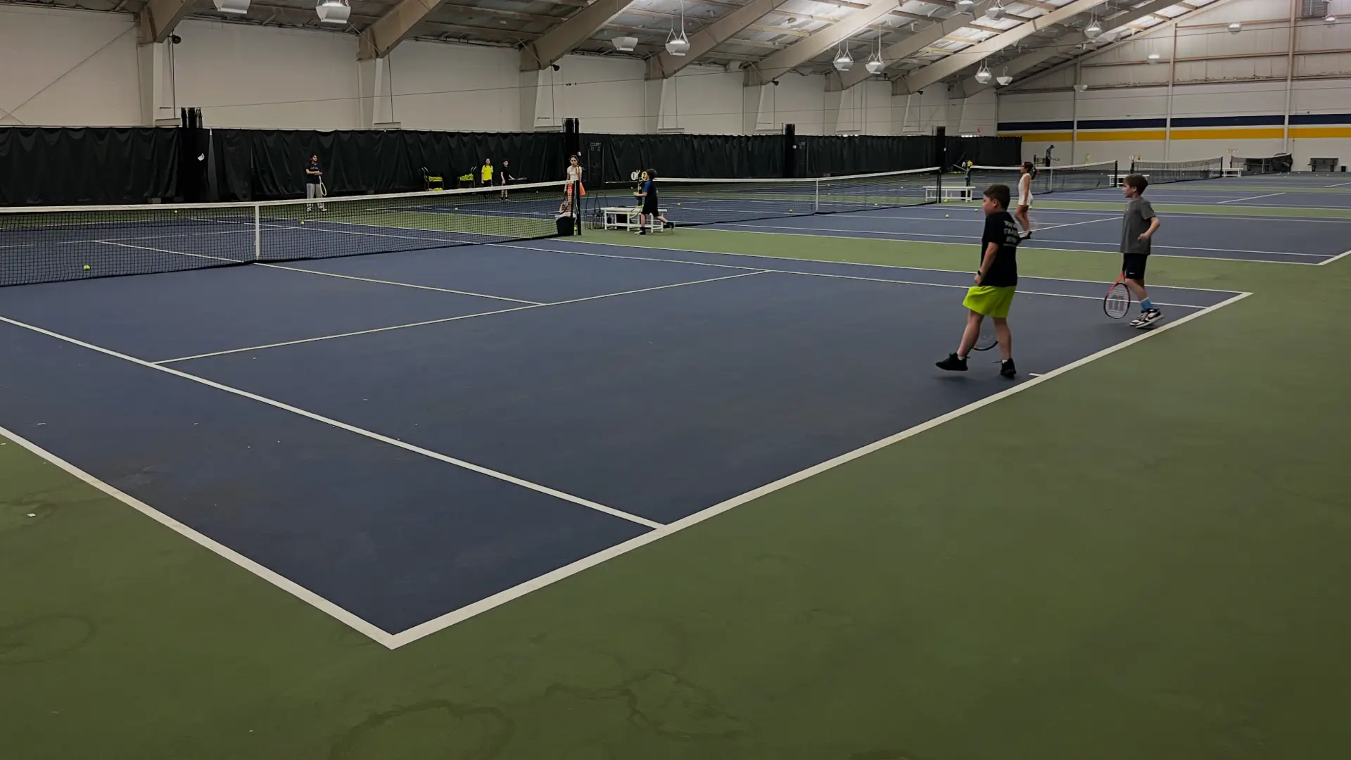 Young players on multiple indoor tennis courts during a tennis session at a TOCA center