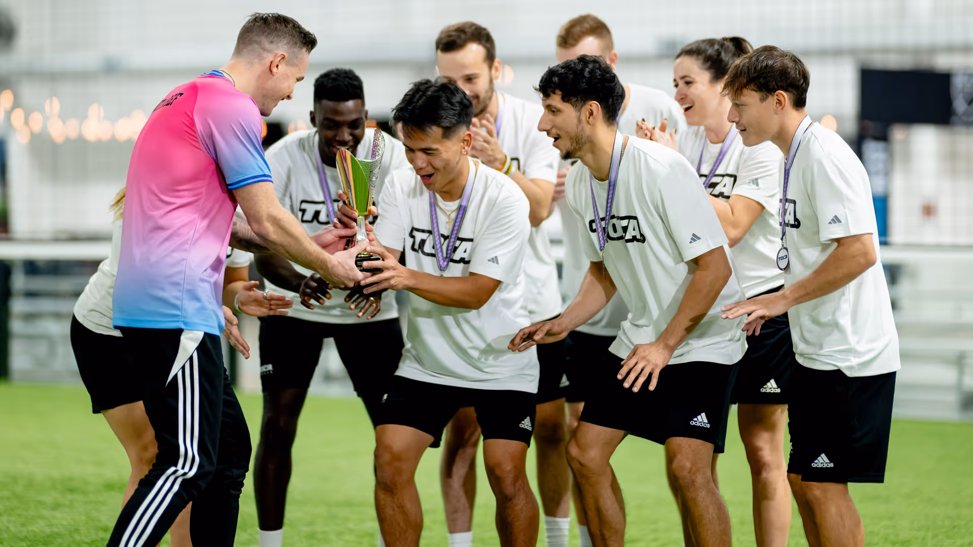Adult soccer players in TOCA jerseys receiving a trophy and medals after winning an indoor soccer tournament at a TOCA Soccer facility