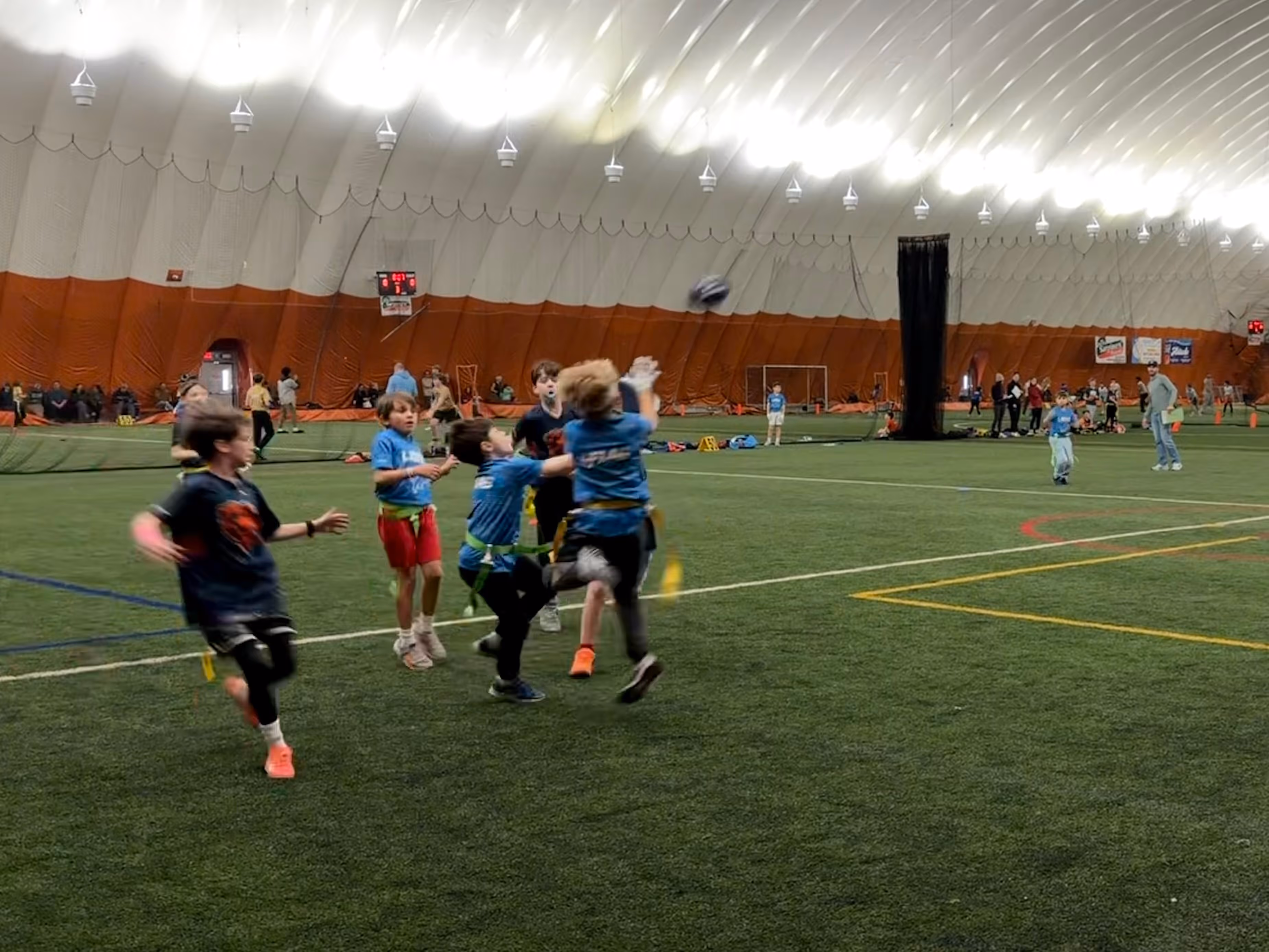 Kids running on an indoor field during an NFL Flag Football game at a TOCA center