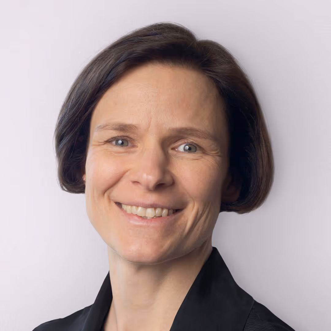 Porträt einer lächelnden Frau mit kurzem braunem Haar vor hellem Hintergrund.