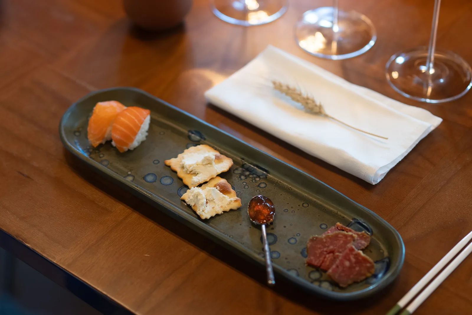 Piattino con nigiri di salmone, cracker al formaggio, confettura e carpaccio accanto ai calici