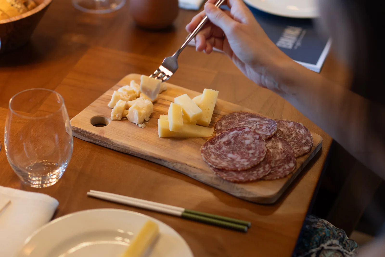 Tagliere di legno con formaggi e salumi artigianali e una mano che serve un assaggio