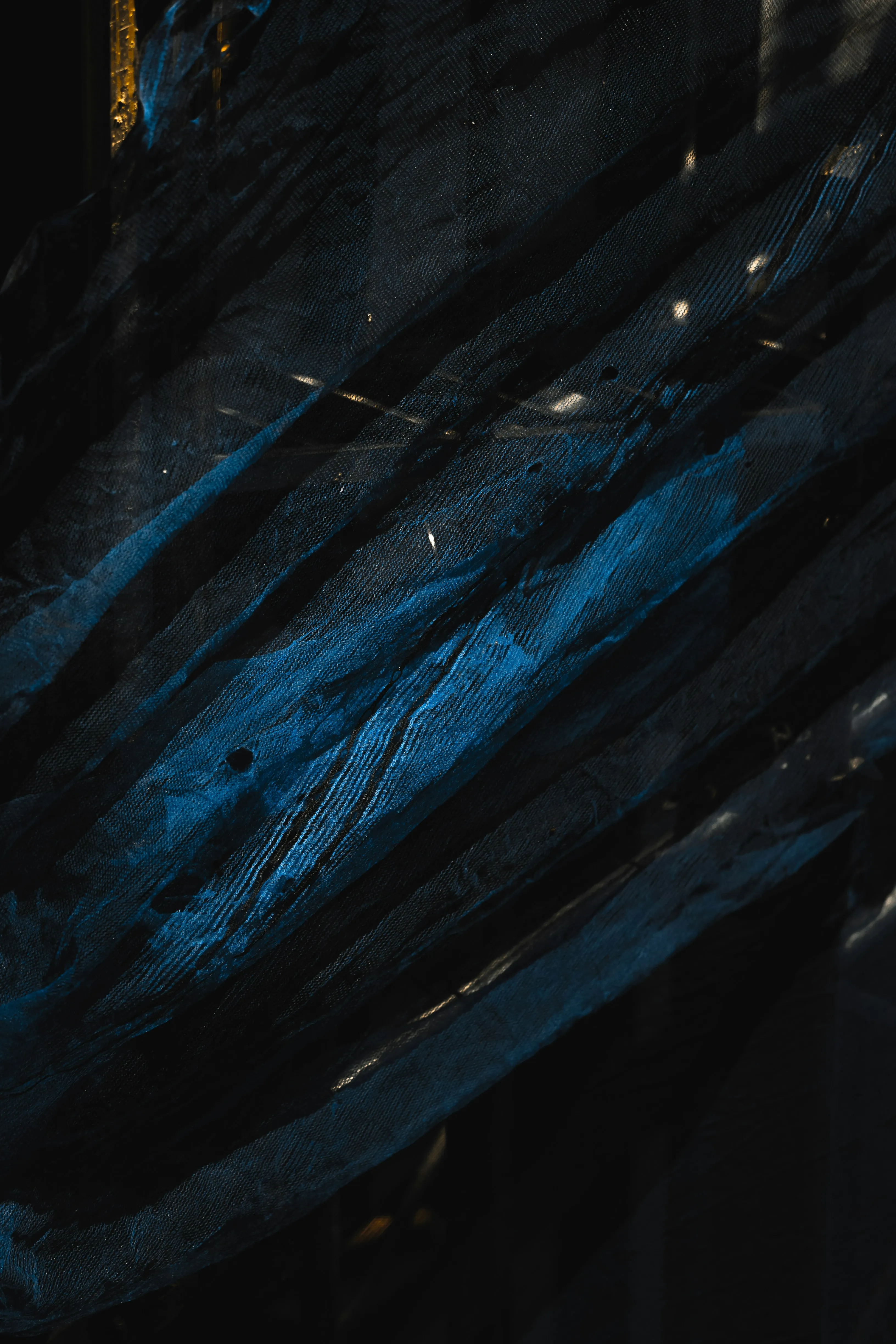 Close-up of dark blue and black sheer fabric with striped patterns and subtle highlights.