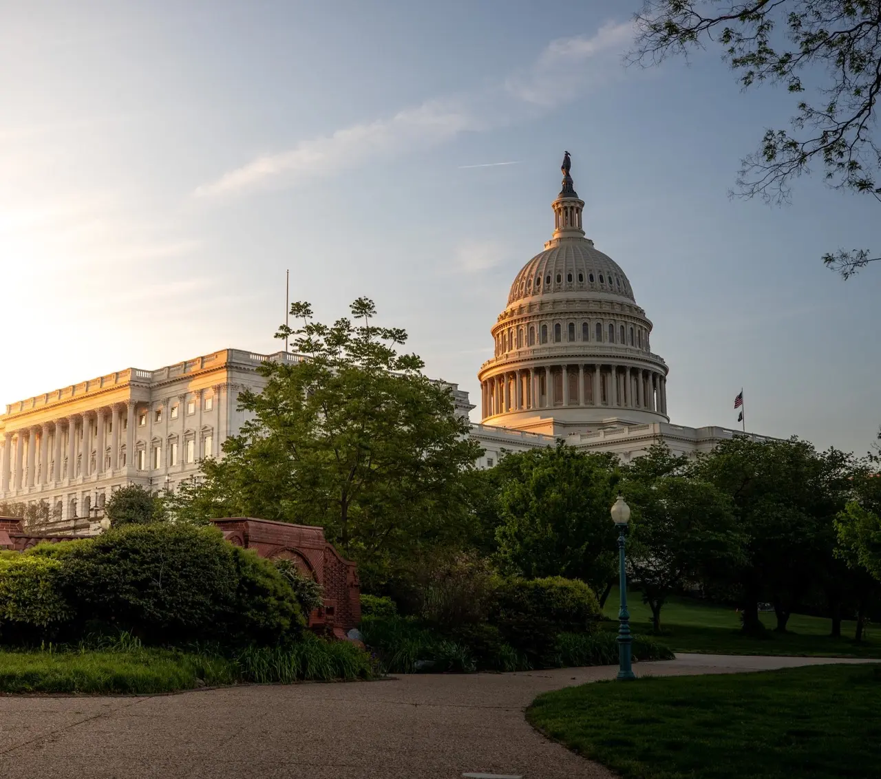 United States Capitol building illuminated by soft evening sunlight with surrounding trees and a clear sky.