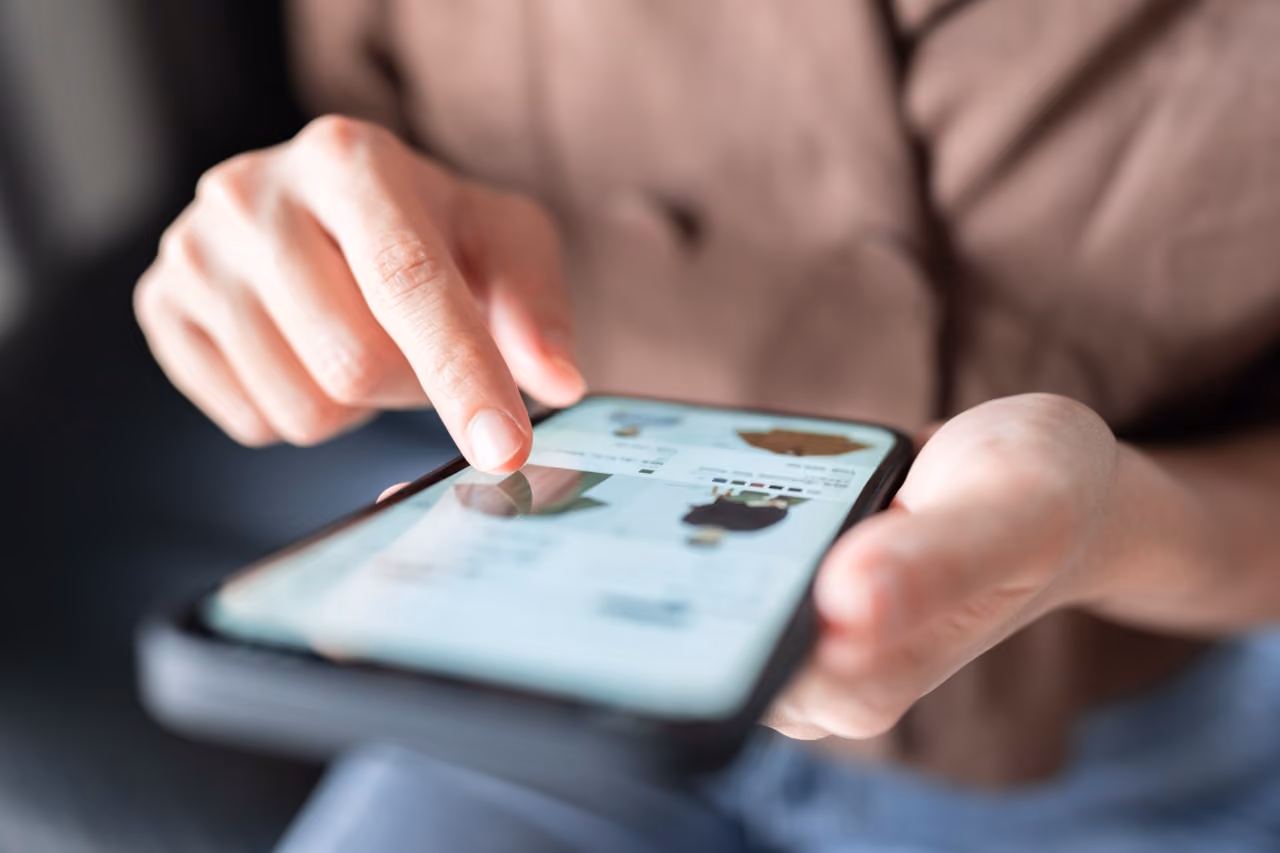 Person shopping online on a smartphone, browsing product images on screen.