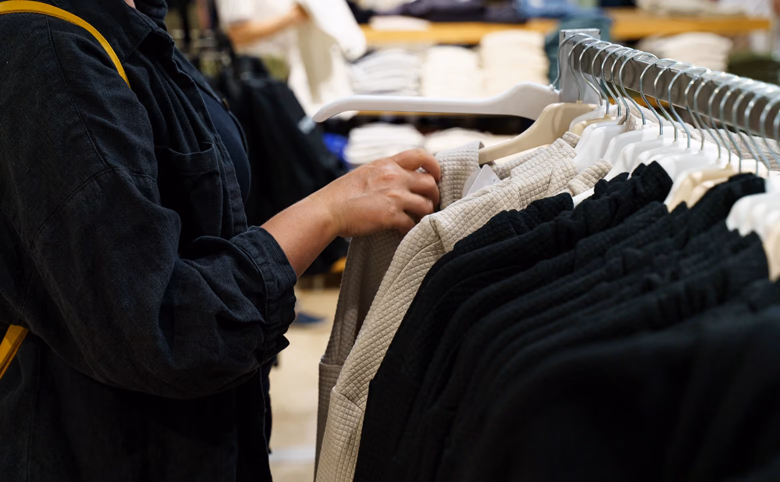 Person browsing textured black and beige jackets on hangers in a clothing store.