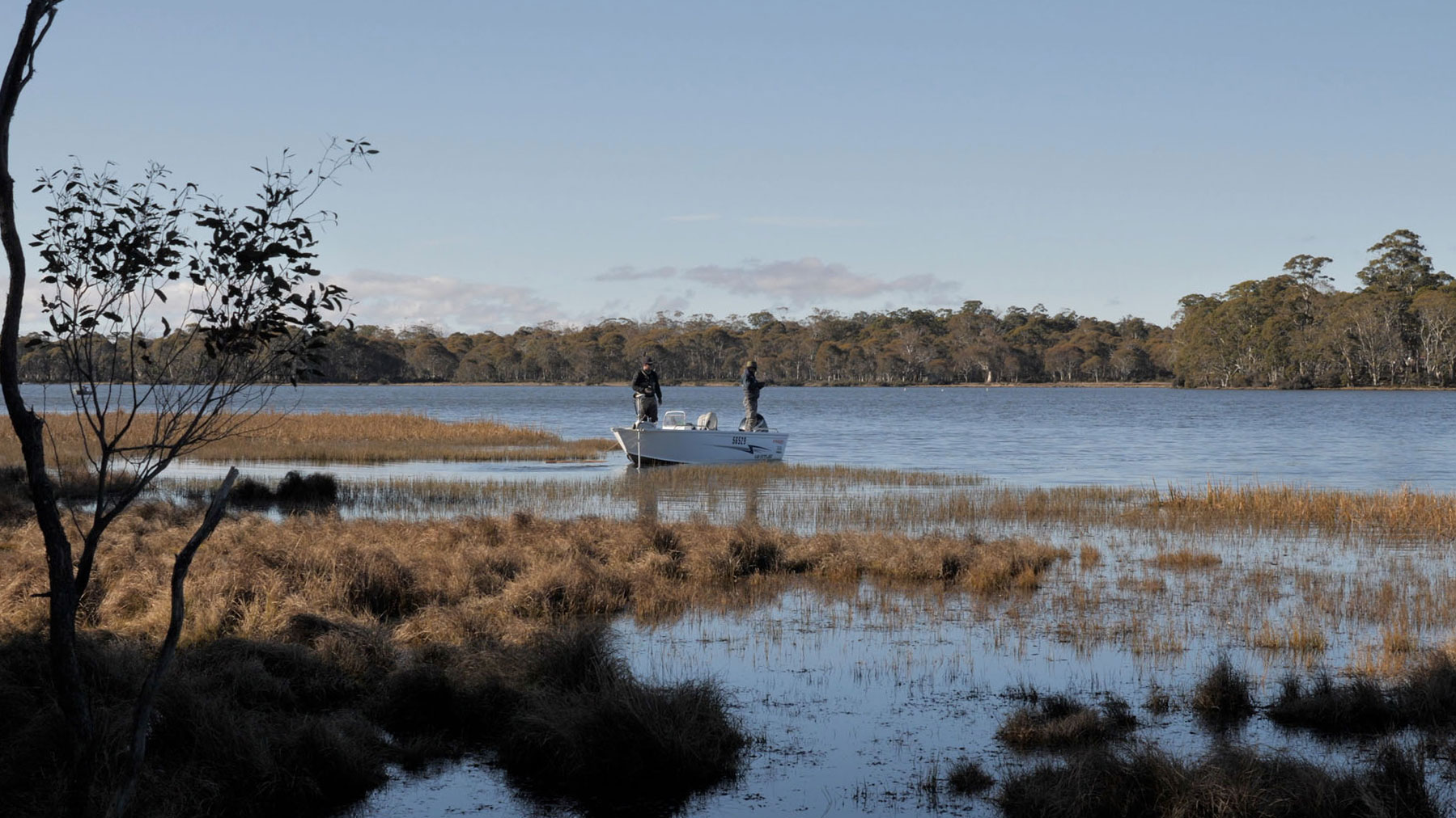 matt and nick in blue tops and fly fishing waders stand on boat on penstock lagoon