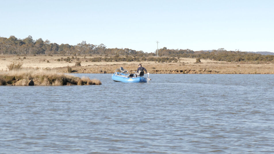 Angler in a blue drift boat fly fishing on a calm Tasmanian lake