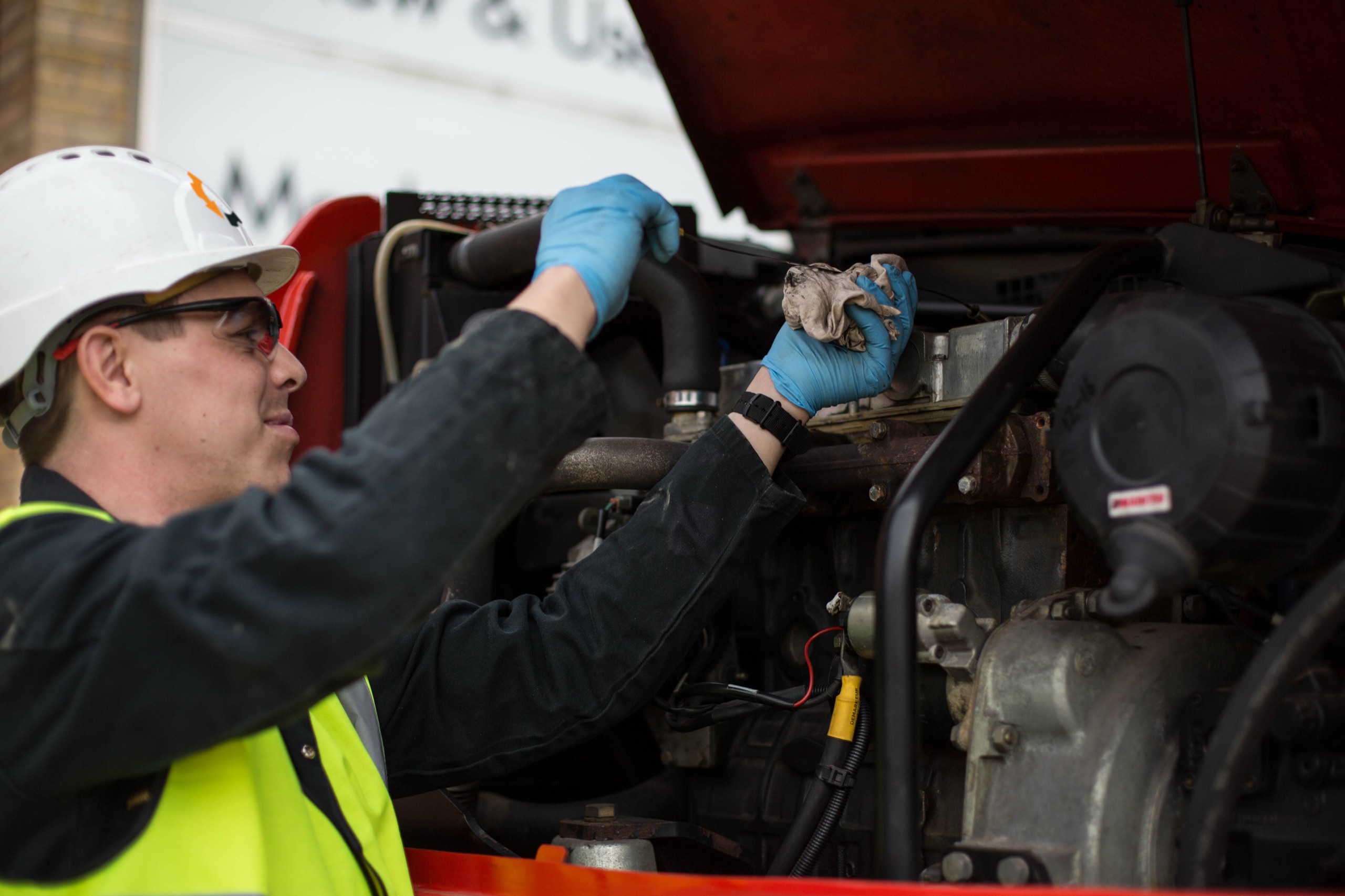 EquipmentShare technician in a hard hat and blue gloves servicing a machine engine