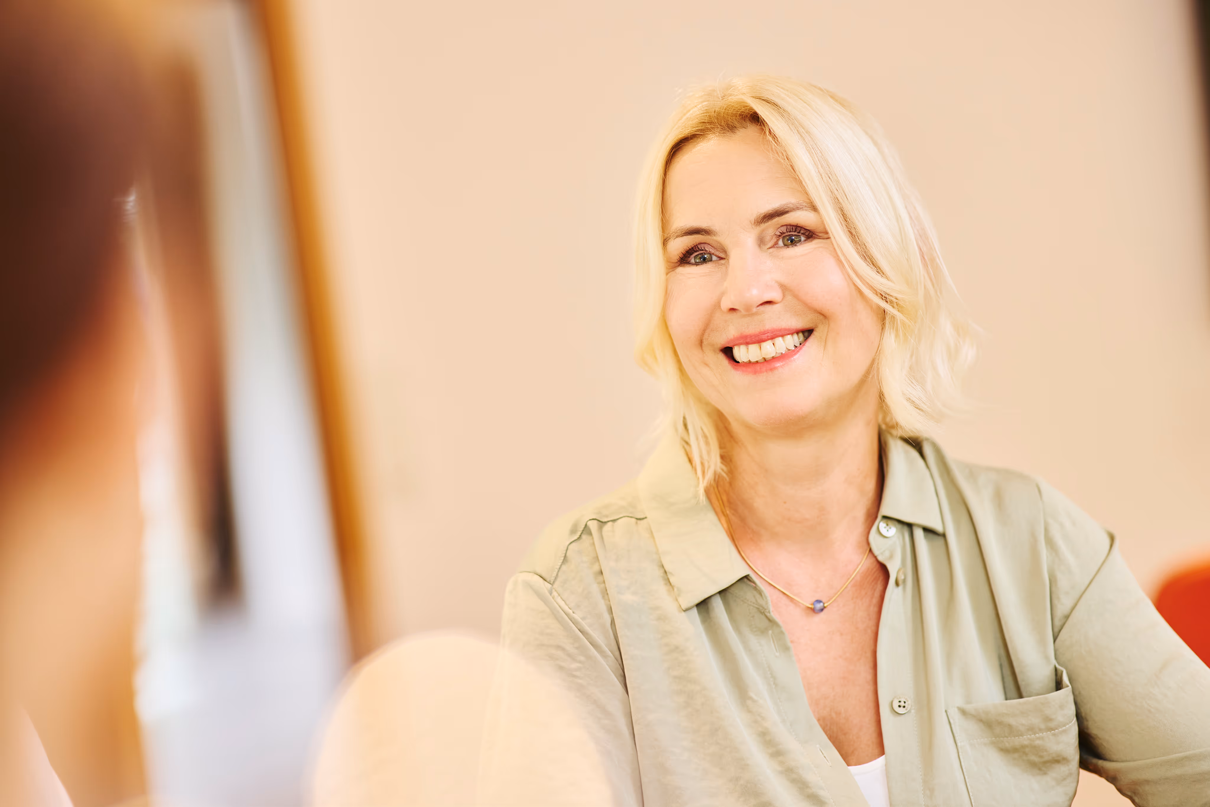 Portrait einer blonden Frau in grüner Bluse, die entspannt und fröhlich wirkt