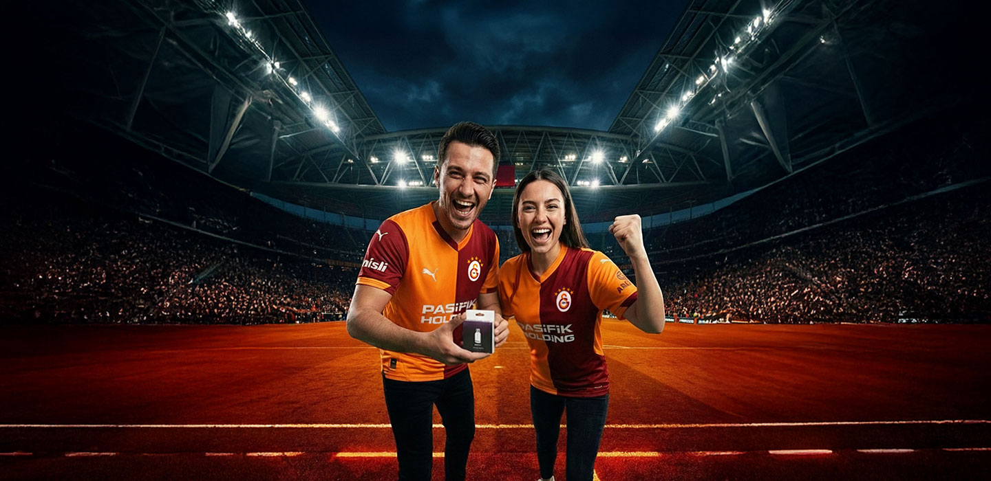 Galatasaray forması giymiş erkek ve kadın futbol stadyumunda kutlama yapıyor, erkek bir kutu tutuyor.