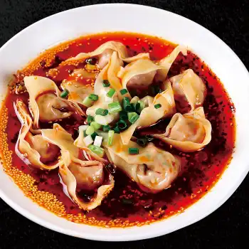 Tender pork dumplings in a tangy sauce, topped with peanuts and sesame seeds