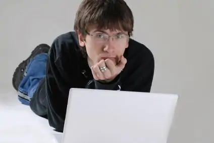 A teenage boy sitting on the floor with his laptop.