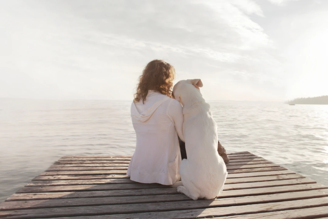 A woman sitting on a dock with her emotional support animal.