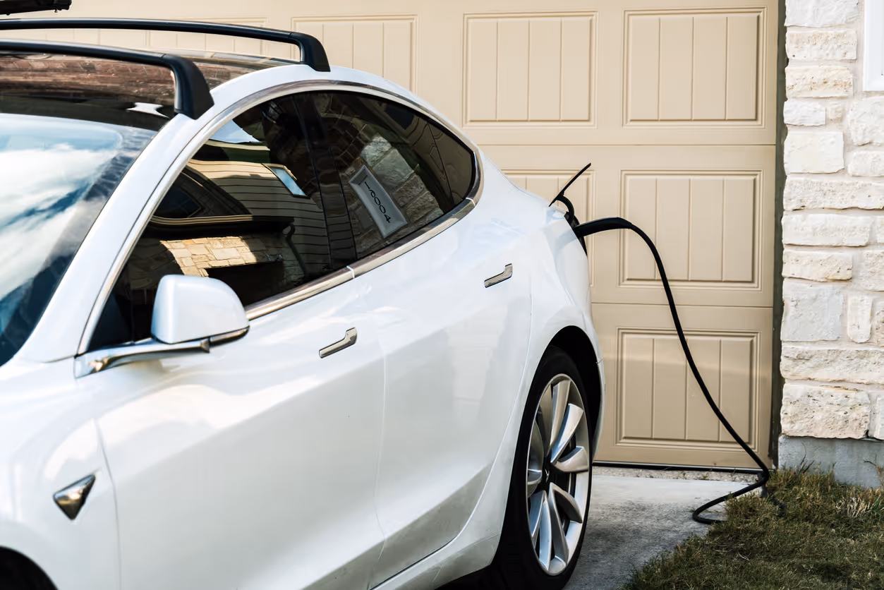 White car charging at a home in front of a garage doot