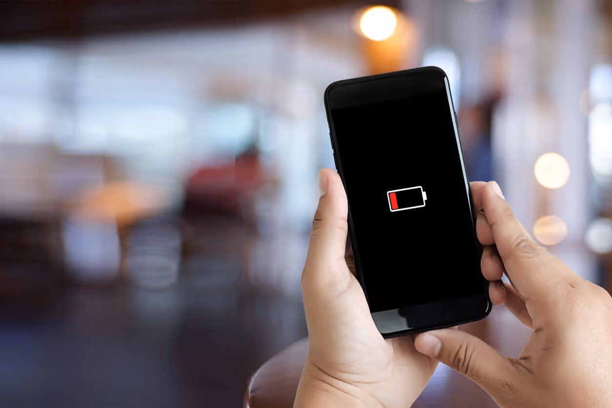 Hands holding a cell phone with a black screen and low battery icon