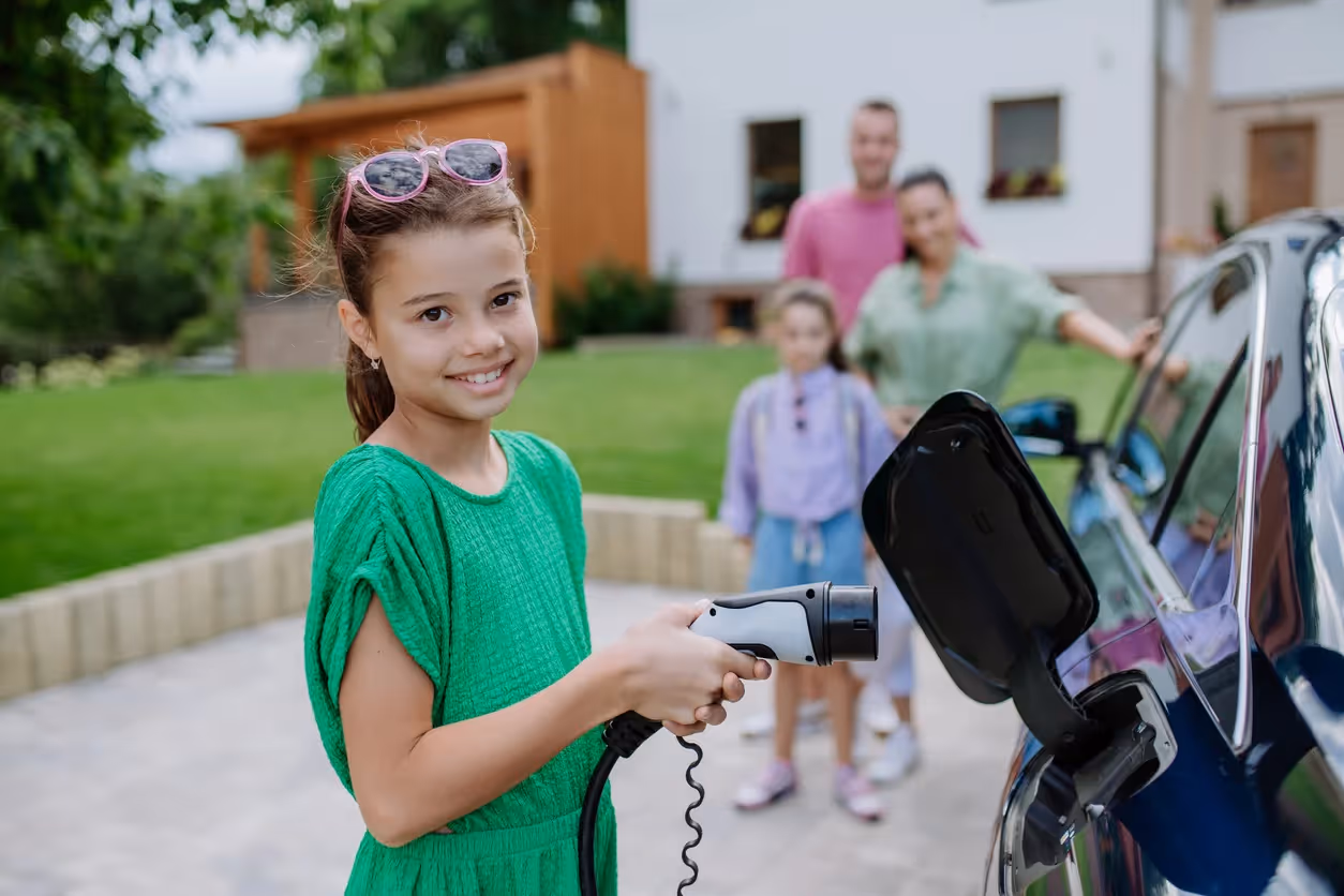 School aged girl holding an EV charger with family in background