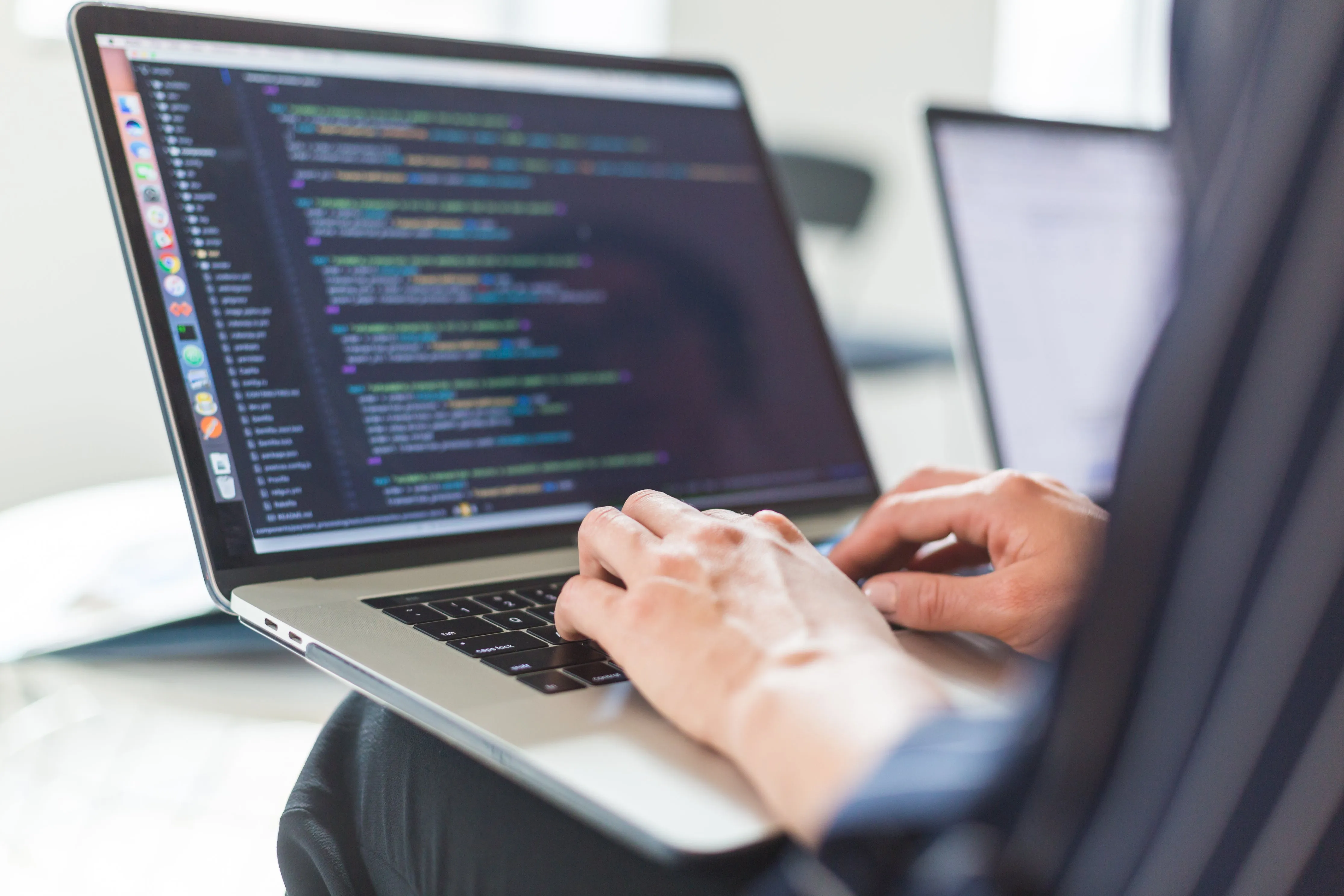 Personne tapant du code sur l'écran d'un ordinateur portable, la syntaxe de programmation étant visible.
