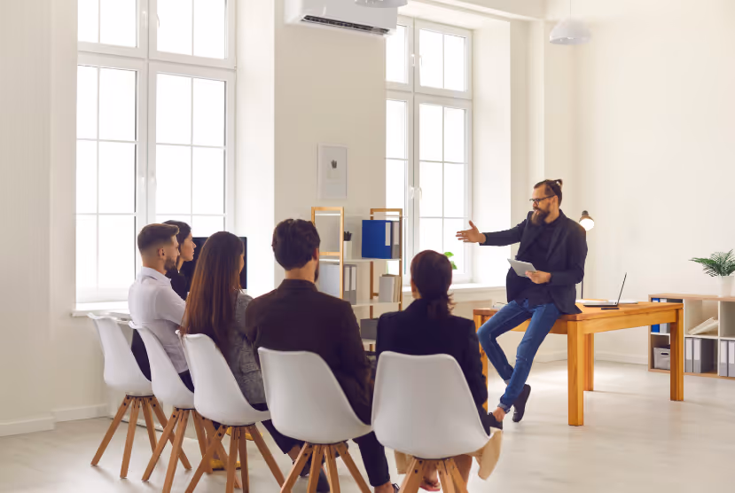 Un homme donne une session de formation en personne à un petit groupe de professionnels dans un bureau moderne.