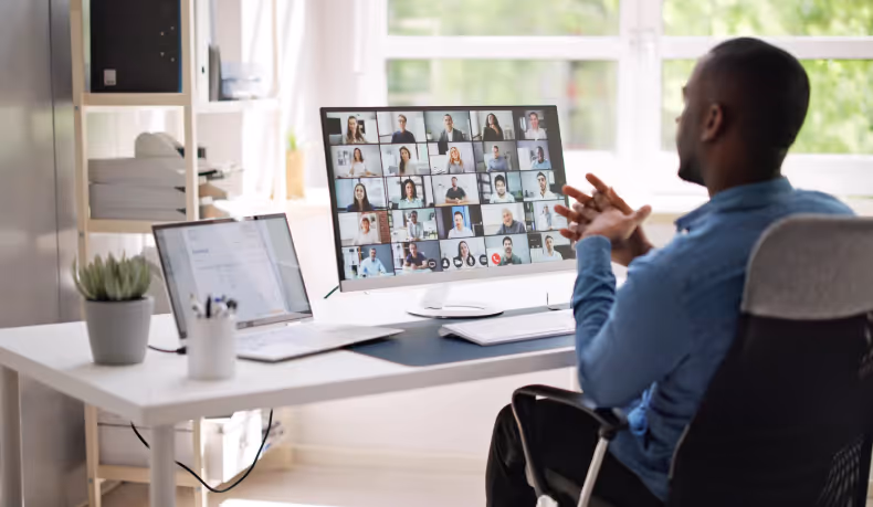 Un homme participe à une grande réunion virtuelle sur un écran d'ordinateur, assis à un bureau moderne.