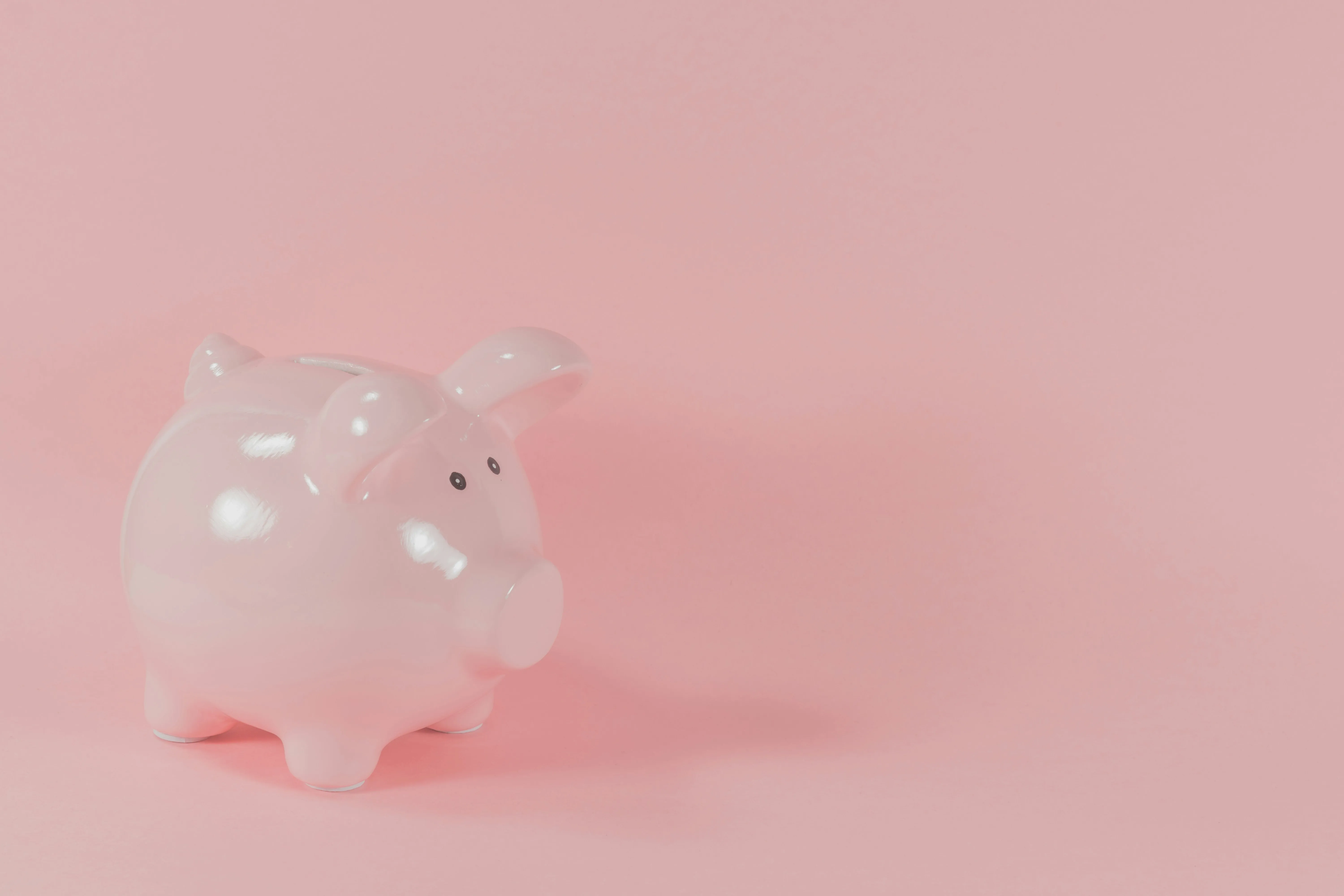 A glossy pink piggy bank sitting on a soft pink background, representing savings and financial planning.