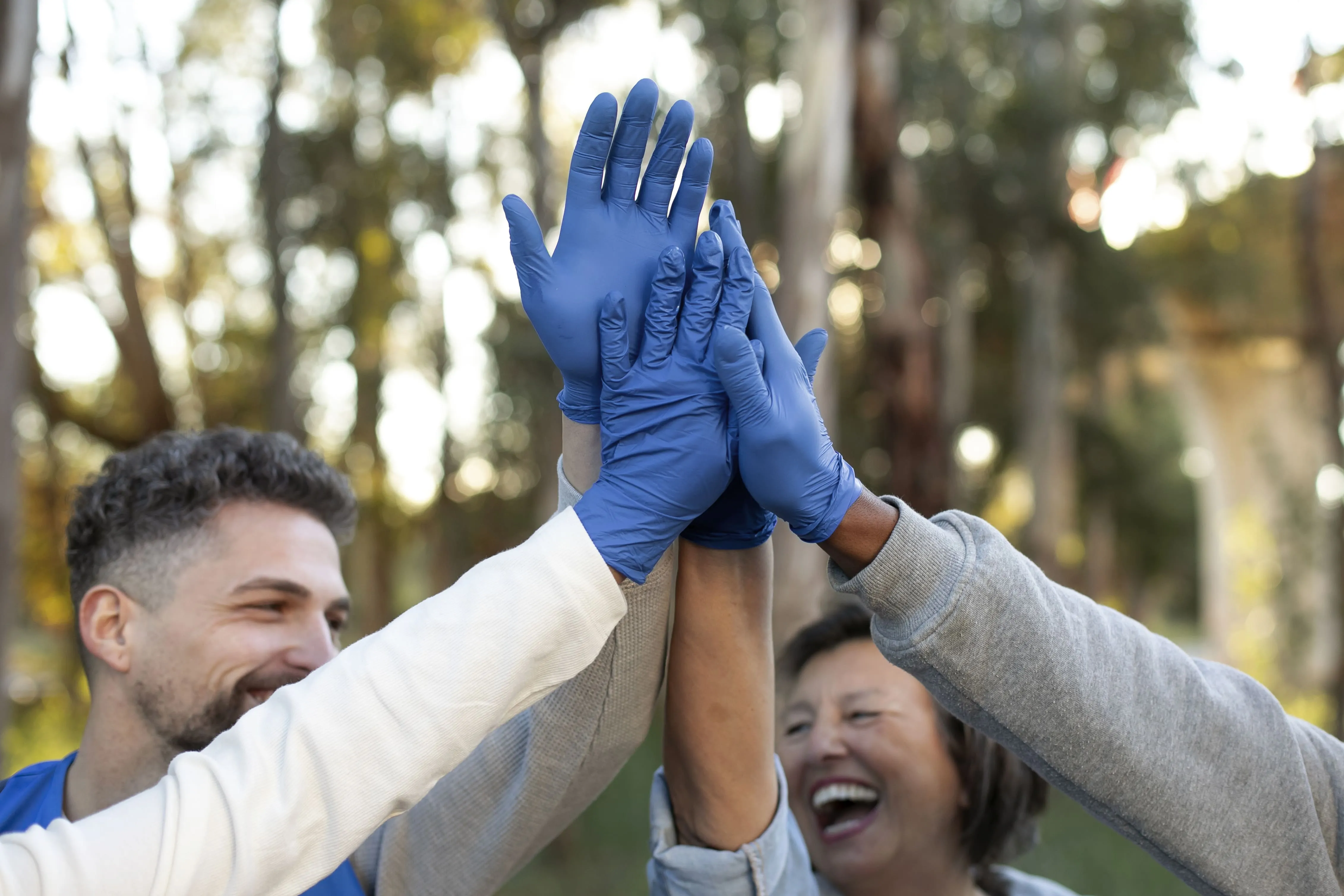 Eine Gruppe von Freiwilligen mit blauen Handschuhen gibt sich im Freien die Hand, lächelt und feiert ihre Teamarbeit.
