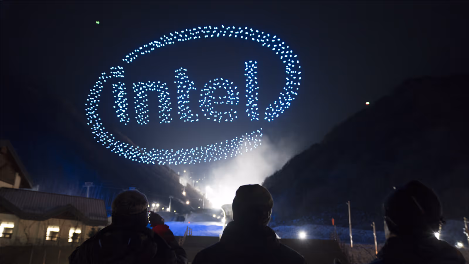 Des personnes regardant un spectacle de drones dans le ciel nocturne formant le logo Intel.