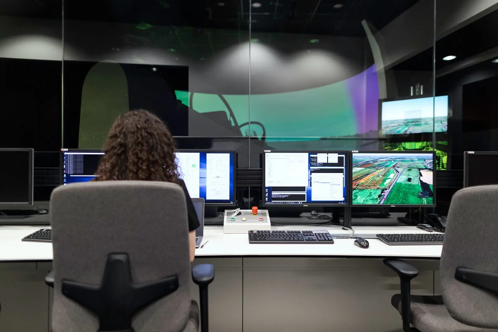 A woman working in a control room with multiple monitors displaying data, code, and satellite imagery in a high-tech environment.