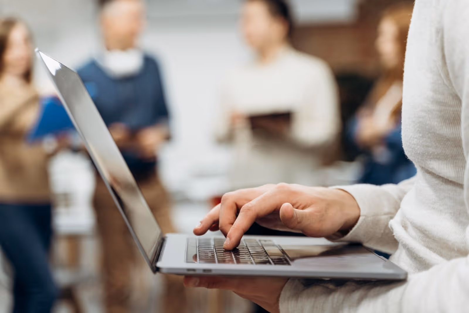 Man typing on a laptop while standing during a group meeting