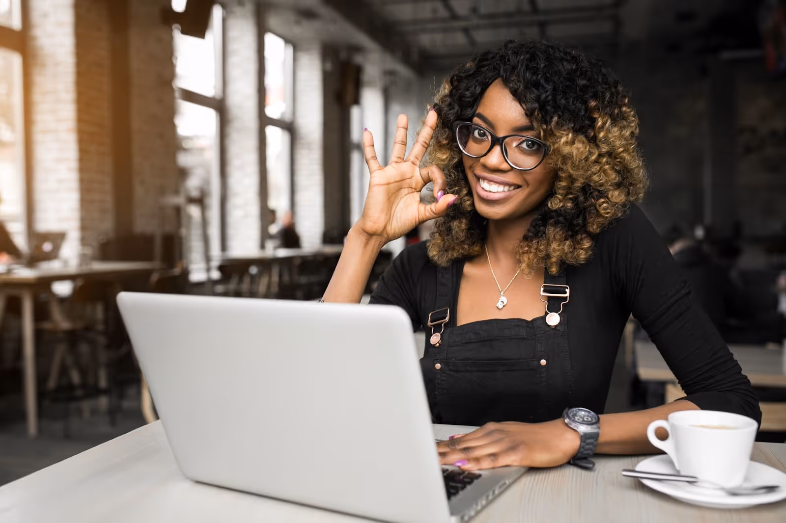 Happy woman in a café making an OK sign while using laptop