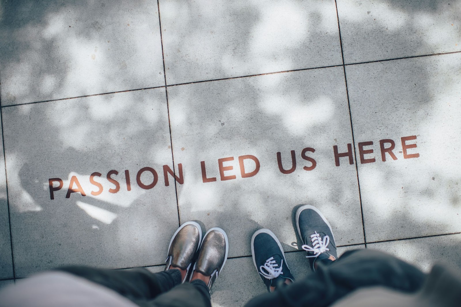 Two people standing on a tiled sidewalk next to the words “PASSION LED US HERE” written on the ground.